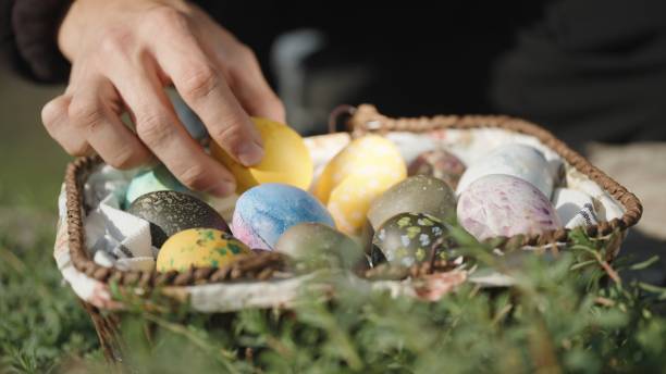 istock Knitted basket with Easter eggs, in the grass. I take and examine the eggs one by one. Close-up. 1875954652