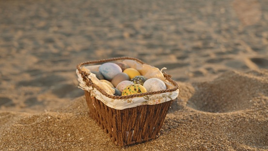 Sea waves and sand are behind. A basket of Easter eggs is in the foreground.