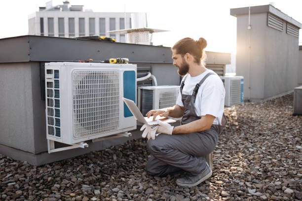istock Repairman looking at conditioner and using laptop on roof 1875959413
