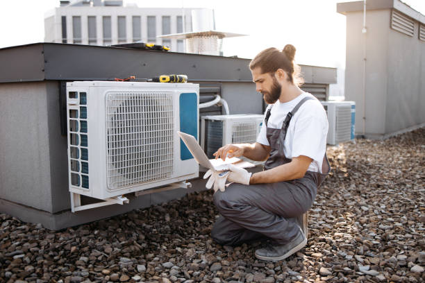 istock Repairman looking at conditioner and using laptop on roof 1875959428