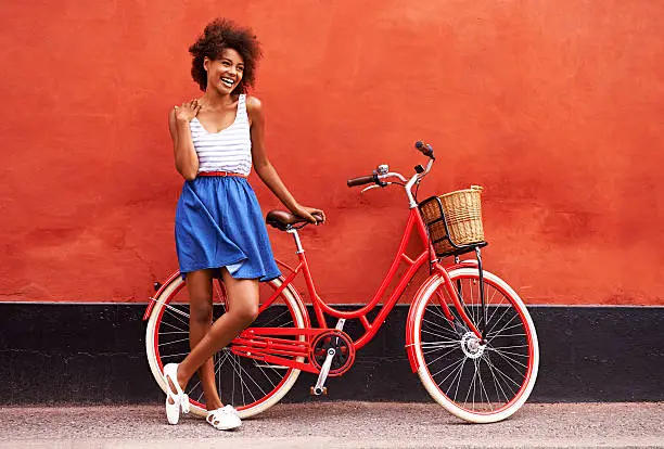 Young smiling woman standing in front of an orange wall with her bicycle