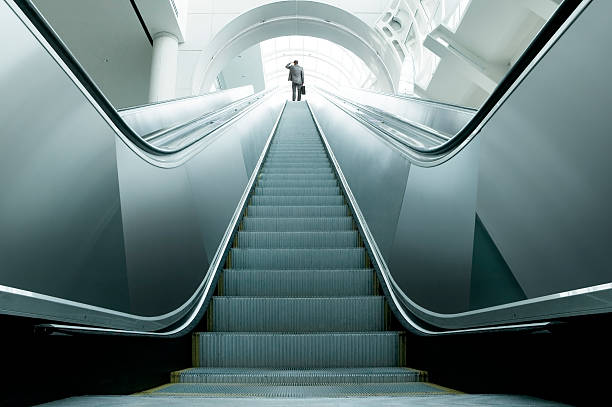 What Next? A businessman at the top of an escalator surveying the possibilities. escalator stock pictures, royalty-free photos & images