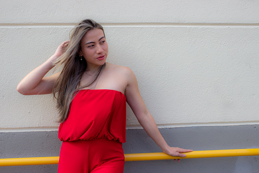 beautiful young woman wearing a red dress posing in front a wall