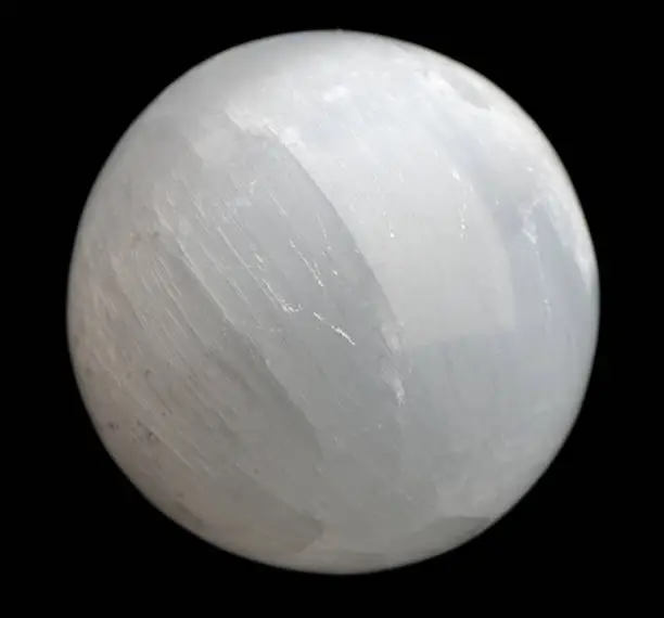 A polished white sphere of selenite, a type of gypsum, against a black background.