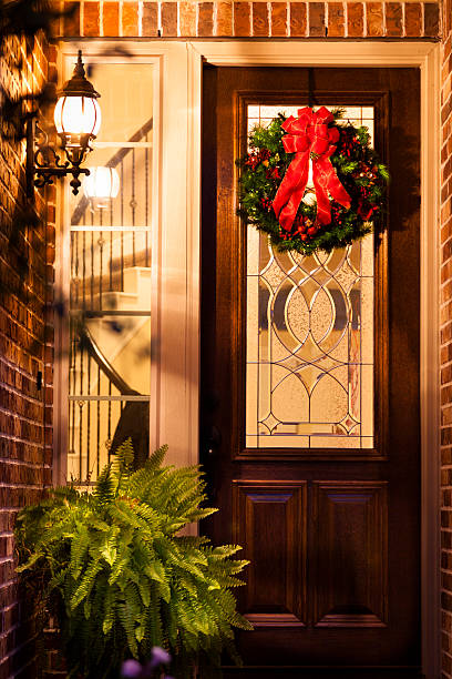 Christmas:  Holiday wreath on front door of home at night. Beautiful holiday wreath on front door of modern, brick home.  Spiral staircase can be seen through window.  Image taken at night...timed exposure. looking out front door stock pictures, royalty-free photos & images