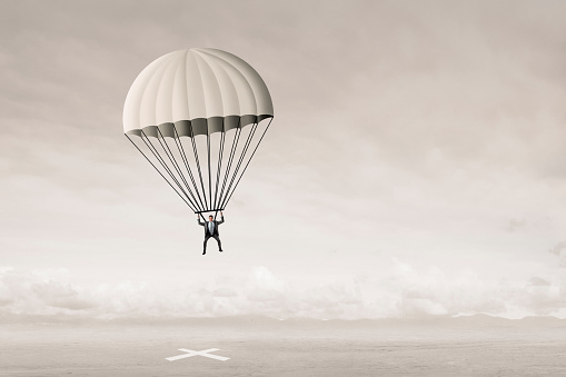 A businessman descends from the sky wearing a parachute as he is about to land on his target.