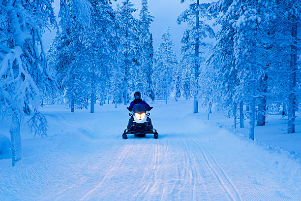 conduire à travers la forêt de motoneige congelé en laponie finlandaise au crépuscule - vibrant color forest ice snow photos et images de collection