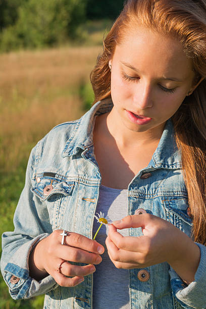 istock Beautiful young woman pulling out daisy petals in field. 187618370