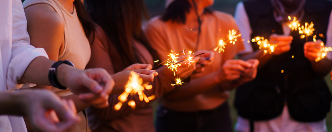Group of Asian young men and women celebrating together with a sparkling firework in the evening. Happy men and women enjoy playing a sparklers firework in a party.