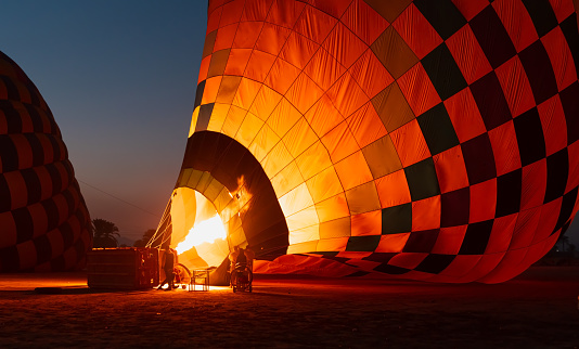 Hot air balloon is inflating before liftoff - Hatshepsut Temple at sunrise in Valley of the Kings and red cliffs western bank of Nile river- Luxor- Egypt