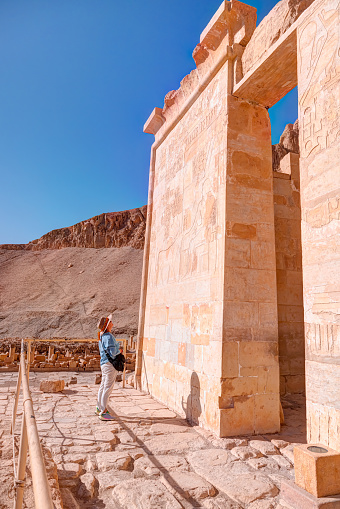A woman looking at hieroglyphs  - Hatshepsut Temple at sunrise in Valley of the Kings and red cliffs western bank of Nile river - Luxor- Egypt
