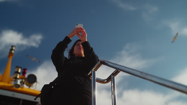 Asian female tourist traveling on ferry and taking photos and videos with her mobile smart phone