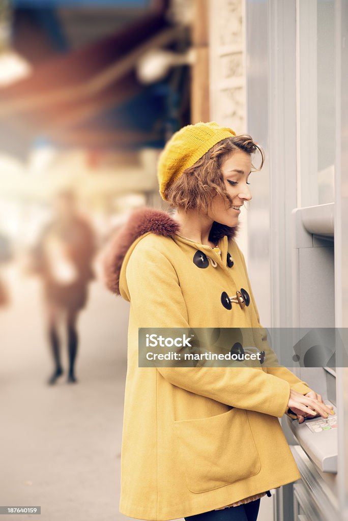 Young woman at ATM machine on street. Young woman in warm clothes at ATM machine on european street. This is from the iStockalypse Paris. ATM Stock Photo