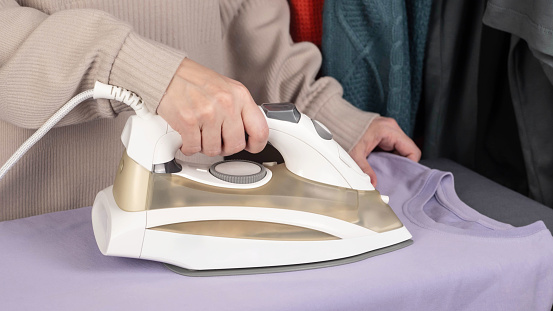 A girl irons clothes with a steam iron on an ironing board. Housework. Modern steam system.