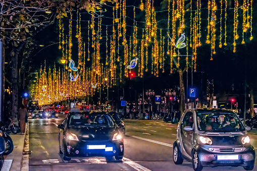 Barcelona, Spain - November 26, 2021: Cars drive along a night road under glowing hanging golden garlands on Passeig de Gracia in Barcelona, Spain. Christmas illumination on a city street in December at dusk