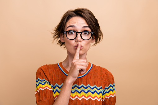 Photo of pretty girl finger touch lips demonstrate shush gesture no talk isolated on beige color background.