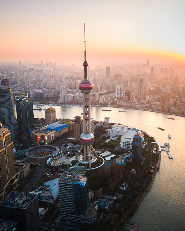 Oriental Pearl TV Tower above Shanghai cityscape lights up during a stunning sunset above the Bund and the new town. This aerial view captures the dynamic skyline, showcasing the modern architectural marvels against the warm hues of the setting sun. Experience the magic of Shanghai's skyline in this captivating moment. China development witness in real time