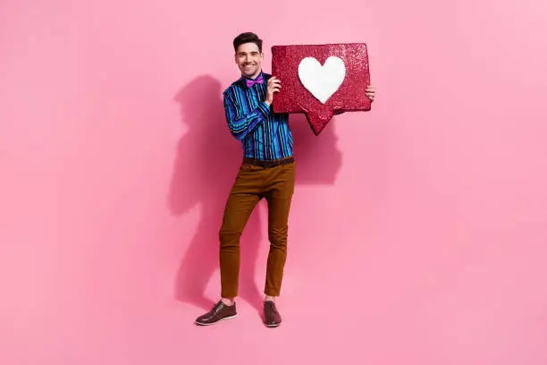 Photo of Full length photo of handsome man hold big red like notification icon recommend you subscribe his blog isolated on pink color background