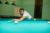 A man plays billiards effectively and hits the ball with a cue. A handsome man leans over a billiard table and makes a precise hit on a billiard ball. Concept of hitting the ball with a cue.