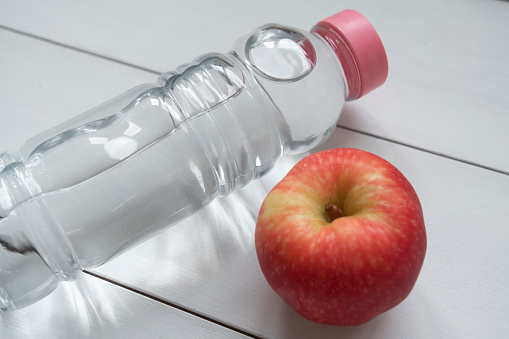 Healthy lifestyle. Apple, water bottle on white wooden.close up.