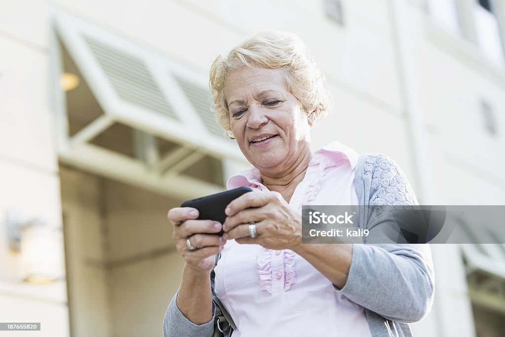 Senior woman texting Senior woman (70s) walking in city, texting. 70-79 Years Stock Photo