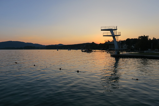 It's a beautiful summer evening in Seewalchen at the Lake Atter in Upper Austria. The sky is colored orange behind the diving tower as a sight of the municipality Seewalchen.