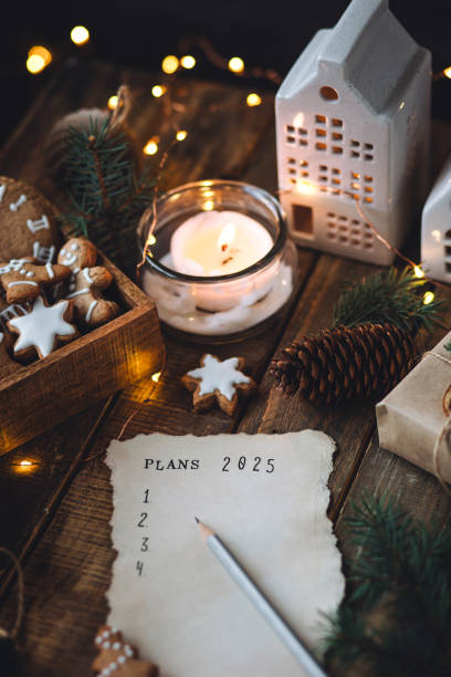 writing new year resolutions 2025 by hand in december on new year's eve. plan, goals, ideas, projects. cozy home holiday atmosphere, christmas lights, festive decor, homemade gingerbread cookies - determination new years eve list aspirations photos et images de collection