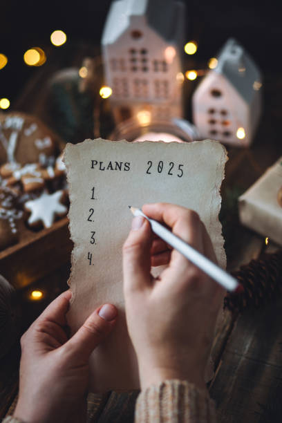 writing new year resolutions 2025 by hand in december on new year's eve. plan, goals, ideas, projects. cozy home holiday atmosphere, christmas lights, festive decor, homemade gingerbread cookies - determination new years eve list aspirations 뉴스 사진 이미지