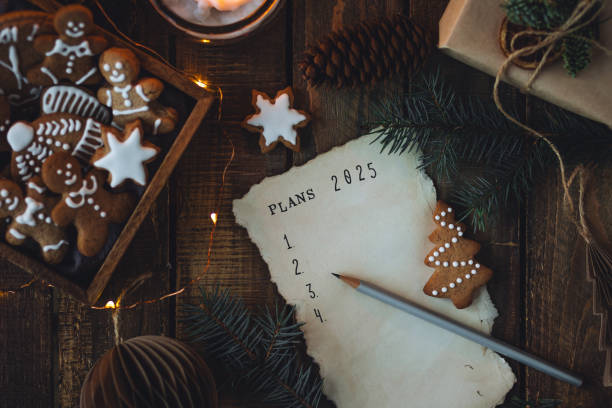 writing new year resolutions 2025 by hand in december on new year's eve. plan, goals, ideas, projects. cozy home holiday atmosphere, christmas lights, festive decor, homemade gingerbread cookies - determination new years eve list aspirations photos et images de collection