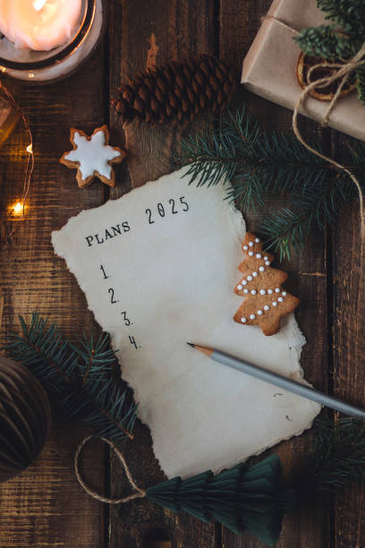 writing new year resolutions 2025 by hand in december on new year's eve. plan, goals, ideas, projects. cozy home holiday atmosphere, christmas lights, festive decor, homemade gingerbread cookies - determination new years eve list aspirations photos et images de collection