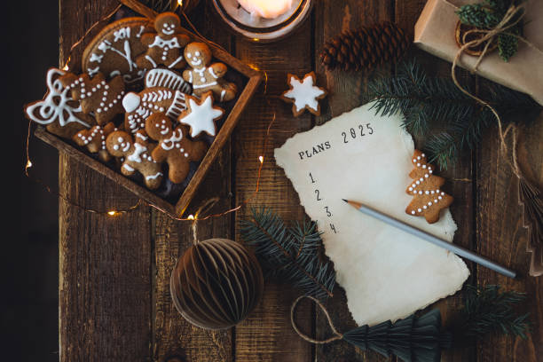 writing new year resolutions 2025 by hand in december on new year's eve. plan, goals, ideas, projects. cozy home holiday atmosphere, christmas lights, festive decor, homemade gingerbread cookies - determination new years eve list aspirations photos et images de collection