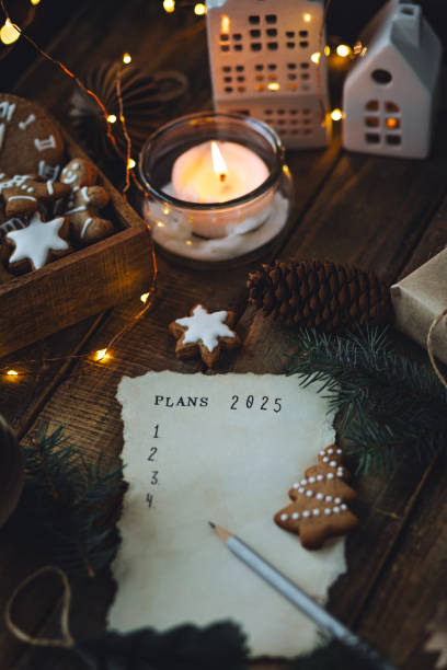 writing new year resolutions 2025 by hand in december on new year's eve. plan, goals, ideas, projects. cozy home holiday atmosphere, christmas lights, festive decor, homemade gingerbread cookies - determination new years eve aspirations letter foto e immagini stock