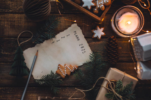 writing new year resolutions 2025 by hand in december on new year's eve. plan, goals, ideas, projects. cozy home holiday atmosphere, christmas lights, festive decor, homemade gingerbread cookies - determination new years eve aspirations letter foto e immagini stock