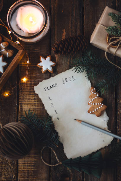 writing new year resolutions 2025 by hand in december on new year's eve. plan, goals, ideas, projects. cozy home holiday atmosphere, christmas lights, festive decor, homemade gingerbread cookies - determination new years eve list aspirations photos et images de collection