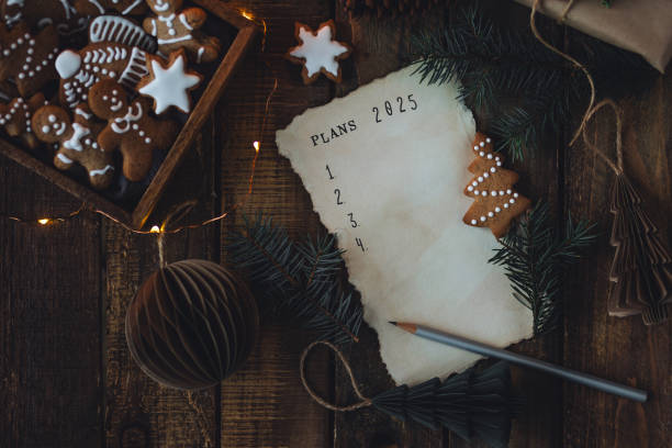 writing new year resolutions 2025 by hand in december on new year's eve. plan, goals, ideas, projects. cozy home holiday atmosphere, christmas lights, festive decor, homemade gingerbread cookies - determination new years eve list aspirations photos et images de collection