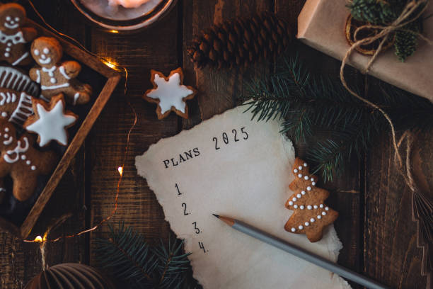 writing new year resolutions 2025 by hand in december on new year's eve. plan, goals, ideas, projects. cozy home holiday atmosphere, christmas lights, festive decor, homemade gingerbread cookies - determination new years eve list aspirations photos et images de collection