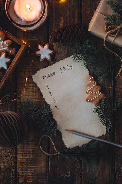 writing new year resolutions 2025 by hand in december on new year's eve. plan, goals, ideas, projects. cozy home holiday atmosphere, christmas lights, festive decor, homemade gingerbread cookies - determination new years eve aspirations letter foto e immagini stock