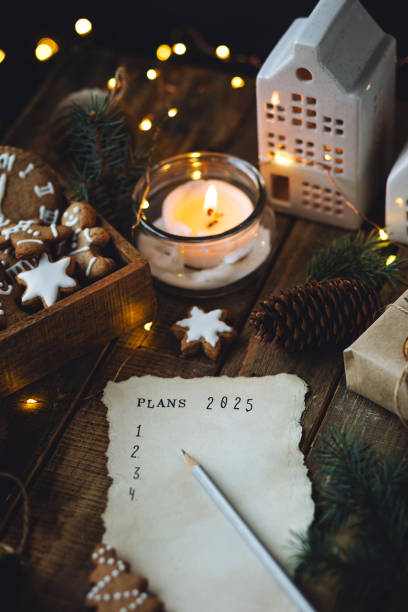 writing new year resolutions 2025 by hand in december on new year's eve. plan, goals, ideas, projects. cozy home holiday atmosphere, christmas lights, festive decor, homemade gingerbread cookies - determination new years eve aspirations letter foto e immagini stock