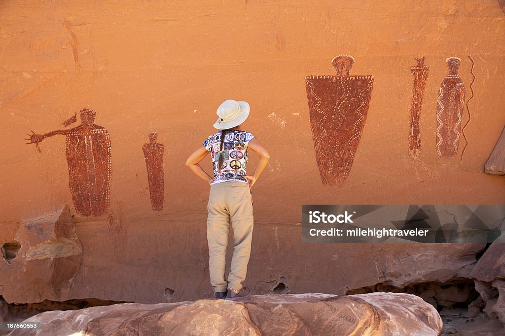 Hiker admires Glen Canyon pictographs Utah A woman admires life-sized Barrier Canyon Style pictographs which remain on the vertical wall of sandstone rock after many hundreds perhaps thousands of years in the Glen Canyon National Recreation Area in southern Utah. The pictographs were made by the Desert Archaic Culture which used the area from about 8000 B.C. to 400 A.D. Adult Stock Photo