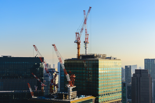 Tower cranes and unfinished buildings, construction cranes on blue sky at construction site in city metropolis.