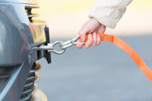 Hand holding tow rope near towing hook assembled to a broken car