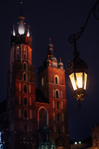 Krakow, Poland - Jan 18, 2018 vintage lantern is illuminate the street. A magnificent old building with two towers in the background.St. Mary's Basilica