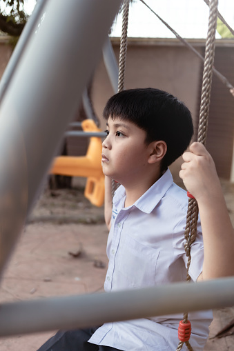A sad lonely little kid sitting alone in the playground.Upset problem child sitting at playground.Concept of bullying, depression, child protection,  loneliness and unhappy children.