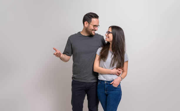 istock Romantic man with arm around girlfriend holding hands and looking at each other on white background 1876720646