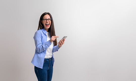 Portrait of happy professional in glasses laughing and pointing at mobile phone on white background