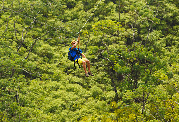 Man with backpack ziplining through a forest Man on Zipline over Lush Tropical Valley flying fox photos stock pictures, royalty-free photos & images