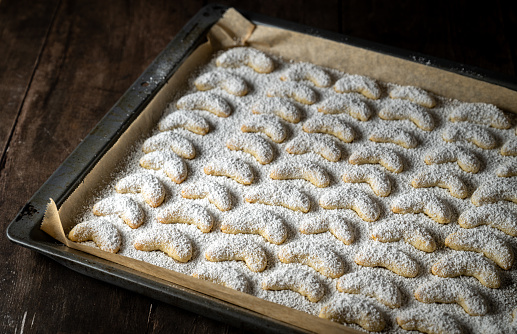 fresh, homemade Christmas pastries, cookies, vanilla crescents sprinkled with powdered sugar on a dark moody background. Selective sharpness on individual cookies