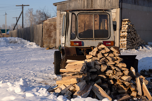 Winter village landscape with firewood and an old tractor at a wooden house