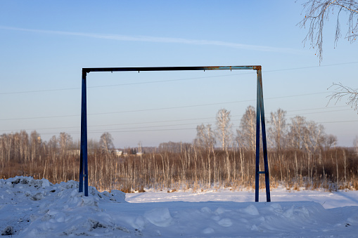 An iron black rack for summer swings on a snow-covered playground. Without a swing