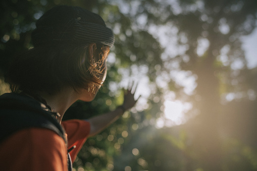 Asian young woman raise hand blocking sunlight in tropical rainforest hiking weekend morning